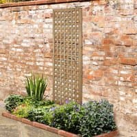 Wooden framed square garden trellis with lattice design, leaning against a brick wall above a flower bed.