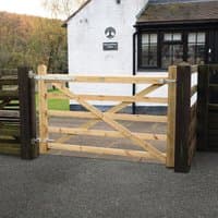 Wooden Croft Prestige gate, 6’x4’, natural finish, diagonal cross-bracing, metal hinges, set between dark posts.