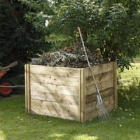 Wooden compost bin with slotted panels, filled with garden waste, next to a rake and wheelbarrow on grass.