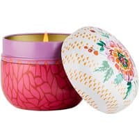 Pink floral Fragonard candle in decorative tin with colorful flower design on lid, lit with a small flame.