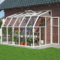 White Palram Canopia Rion 6x10 sunroom with clear panels, attached to brick wall, featuring plants inside.