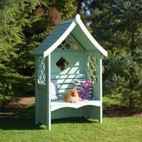 Light green wooden garden arbour seat with lattice sides, sloped roof, and decorative pillows.